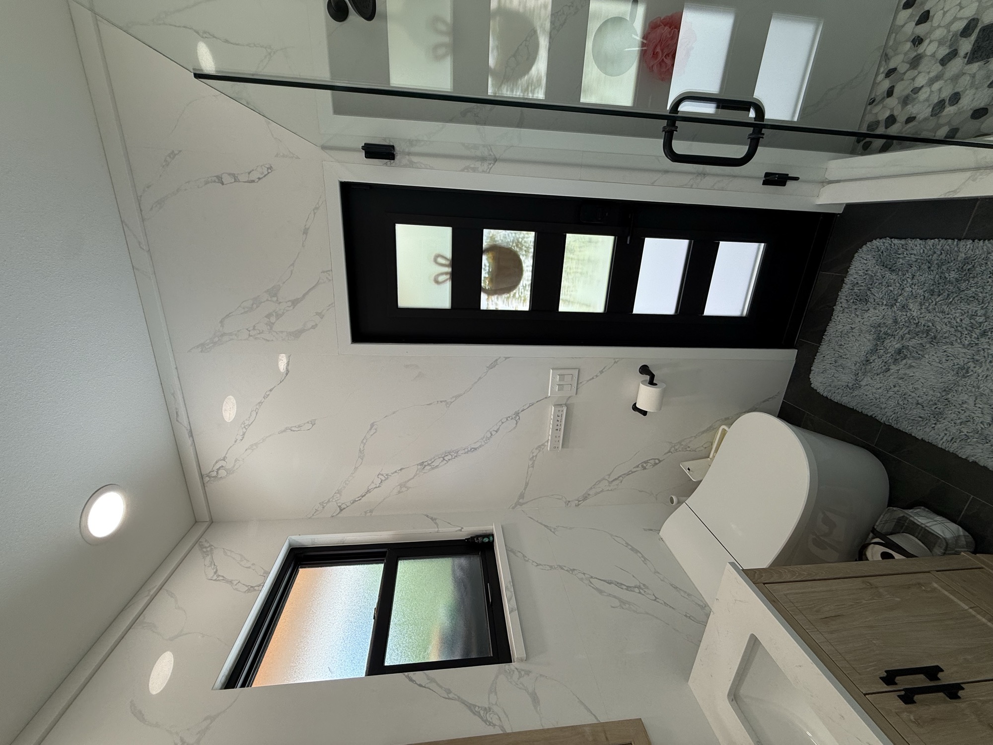 Bathroom with veined light wall surfaces, a wood vanity, black-framed window and door, and glass shower enclosure
